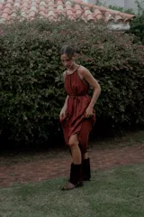 Vestido largo color marrón de crepé plissé, con escote halter adornado con detalles de perlas, silueta fluida y lazo ajustable en la cintura.