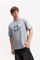 Remera oversize de manga corta, color gris, con calce amplio y estampa frontal con letras en relieve visual y marca Mistral.