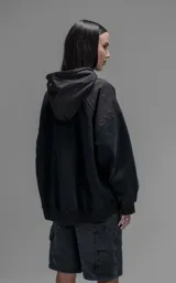 Hoodie oversize color negro, confeccionado en frisa gamuzada de algodón. Presenta capucha forrada en microfibra, mangas raglán y un bolsillo frontal tipo canguro con un bolsillo pequeño superpuesto con solapa.