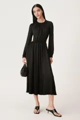 Vestido midi negro de cuello redondo y manga larga abullonada con puños elásticos. Presenta cintura elastizada y espalda descubierta con cierre de botón en el cuello.