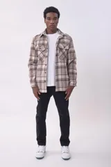 Sobrecamisa de corte holgado con diseño a cuadros en tonos beige y marrón, confeccionada en tejido de textura suave. Presenta cuello clásico, cierre frontal con botones, dos bolsillos con solapa en el pecho y puños abotonados.