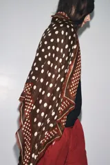 Pañuelo cuadrado de mezcla de tejidos y lana, color marrón oscuro con estampado de lunares beige. Presenta un borde con franjas y lunares más pequeños, y terminaciones deshilachadas.