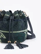Bandolera tipo bucket bag confeccionada en gamuza color verde oscuro con bordados decorativos en hilo claro. Presenta cierre de cordón ajustable con borlas en los extremos, correa larga regulable de cuero y detalles metálicos dorados.