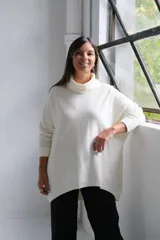 Polerón de punto color crudo, con cuello alto tipo polera, corte holgado y mangas largas con puños acanalados.