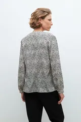 Blusa beige con estampado de lunares negros, cuello en V y mangas largas.
