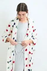 Bata de estar por casa confeccionada en tejido de poliéster suave, con diseño estampado de corazones en colores rojo, negro y verde sobre fondo blanco. Presenta un corte holgado, mangas largas y bolsillos frontales.