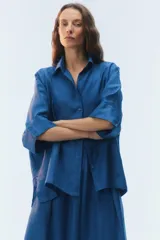 Camisa oversize blanca de lino, con corte cuadrado, mangas raglán cortas con puños anchos, aberturas laterales y cierre frontal de botones.