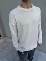 Sweater de tejido de punto color beige con diseño de corte holgado, cuello redondo y detalles de terminaciones desflecadas y roturas en el cuello, puños y ruedo.