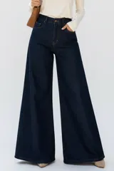 Jeans oxford de mezclilla azul oscuro, tiro alto, con bolsillos laterales y traseros, y perneras amplias y acampanadas.