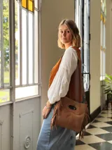 Cartera bandolera de cuero color camel, con forro interno de tela y flecos laterales.