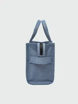 Bolso tipo tote de lona color beige de la marca Marc Jacobs. Presenta el texto 'THE TOTE BAG' estampado en el frente en color blanco, dos asas de mano superiores y una correa de hombro ajustable y removible en color negro.