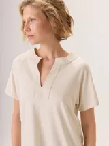 Remera de manga corta color beige claro con brillo sutil (lurex), cuello redondo con abertura en V y cuello mao.