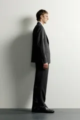 Pantalón de traje slim fit para hombre, color gris oscuro, con bolsillos frontales y bolsillos traseros de doble vivo con botón. Cuenta con cierre frontal de cremallera y botón, y presillas para cinturón.