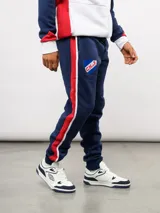 Pantalon de jogging azul de felpa, con franjas laterales en blanco y azul marino. Presenta el escudo del Club Nacional de Football en el muslo derecho y el logo de Umbro en el izquierdo.