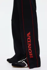 Pantalón jogger negro de corte relajado, con cordón ajustable en la cintura, franjas laterales rojas y estampado con la palabra "Honda" en la pierna izquierda.