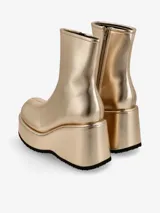 Bota corta dorada, estilo botín, con caña ajustada y punta redonda. Presenta una plataforma y taco cuña muy altos, con suela dentada negra.