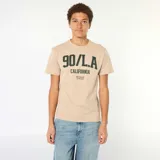 Camiseta de algodón color beige con cuello redondo y mangas cortas. Presenta un estampado frontal en color verde oscuro con la inscripción '90/L.A. CALIFORNIA' y el texto 'FROM THE BLOCK TO THE BEACH'.