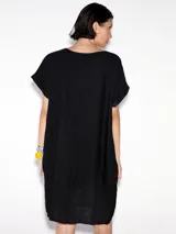 Vestido negro de lino, corte recto, con cuello redondo y mangas cortas. Presenta botones decorativos en la parte inferior.