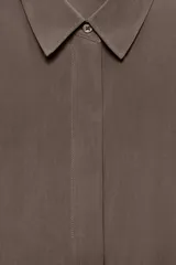 Camisa de corte fluido con cuello solapa y manga corta con dobladillo. Presenta un cierre frontal con botones ocultos bajo una tapeta y un diseño con bajo ligeramente más largo en la parte posterior.