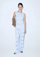 Chaleco celeste de punto con diseño de flores perforadas, sin mangas, escote redondo y cierre frontal con botones.
