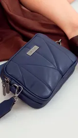 Bandolera de diseño acolchado con costuras geométricas, color verde oliva. Cuenta con doble compartimento con cierre metálico, placa metálica con logo en el frente y correa de cinta ajustable y extraíble.