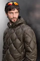 Campera puffer verde oliva acolchada con diseño de rombos, capucha y cierre frontal con cremallera. Incluye bolsillos laterales con cierre. Relleno de plumón y plumas.