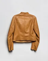 Campera estilo motero de símil cuero color habano, con cuello mao, cierre frontal, calce entallado y detalles de tachas en hombros y mangas.