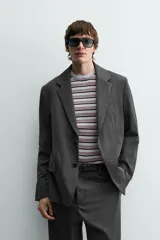 Blazer oversized fit de hombre, color gris oscuro con rayas verticales finas. Cuello con solapas de muesca, manga larga con puño abotonado, bolsillos de solapa en la cadera y bolsillo interior. Cierre frontal de un botón y abertura en el centro de la espalda.