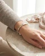 Esclava rígida de acero con baño de oro y detalle de circonia incrustada. Diseño minimalista con grabado.