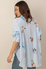 Camisa de corte oversize, con estampa a cuadros vichy en celeste y blanco, complementada con llamativos motivos florales bordados y de manga larga.