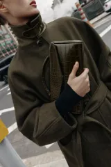 Bolso de mano de formato alargado con textura de efecto cocodrilo. Cuenta con asa de mano superior, asa extraíble para usar como bandolera, bolsillo interior con cierre y cierre frontal mediante clip metálico.