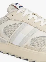Zapatillas Tommy Jeans de estilo running, color blanco hueso, con exterior de ante, interior de poliéster y suela gruesa de goma con tacos. Presentan paneles con mezcla de texturas y detalles distintivos de la marca.