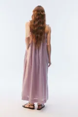 Vestido maxi solero amplio y largo de color amarillo, con escote redondo, frunces que otorgan vuelo, breteles finos ajustables con nudo en los hombros y bolsillos laterales.