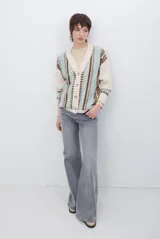 Cardigan de punto con escote en V y cierre frontal de botones. Presenta un diseño estampado con patrones geométricos en tonos beige, marrón y detalles en azul vibrante.