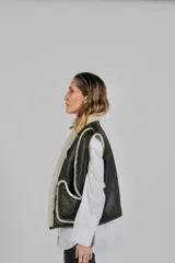 Chaleco reversible confeccionado en lambskin, con una cara de cuero en color marrón oscuro y otra de lana blanca. Presenta bolsillos frontales aplicados con ribetes de lana en contraste y diseño de cuello abierto.