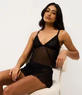 Conjunto de pijama tipo short doll compuesto por una blusa con escote en V y breteles regulables, y un short con cintura elástica. Ambas piezas están confeccionadas en tul transparente con delicados detalles de encaje en el escote y el ruedo.