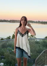 Blusa tipo lencera de satén color crema con escote en V y ruedo asimétrico, ambos decorados con encaje negro. Presenta breteles finos ajustables.