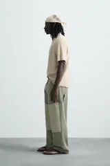 Camiseta de punto color beige claro, corte boxy fit, con cuello redondo y manga corta. Presenta un estampado central en tono similar que simula un efecto spray y acabados irregulares en los bordes.