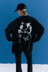 Buzo oversize de cuello alto confeccionado en frisa, con hombros caídos y bolsillos delanteros. Presenta una estampa artística en la espalda con motivos orientales, incluyendo un pez koi, flores y una mariposa.