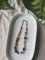Collar corto compuesto por una mezcla de cuentas de cerámica, vidrio, cristal checo y acrílico en tonos multicolor, complementado con una cadena de eslabones metálicos plateados.