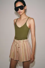 Bermuda de tiro medio con diseño de rayas verticales en tonos rosados y beige. Presenta cintura con trabillas, cinturón ajustable con lazada, bolsillos laterales y detalle de pliegues en el delantero.