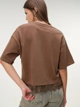 Remera boxy de manga corta marrón, de corte holgado y diseño liso, con detalle de encaje a tono en el borde inferior.