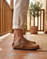 Zuecos de gamuza color marrón con detalle de hebilla lateral y tachas metálicas aplicadas.