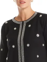 Chaqueta tejida de punto color negro, con cuello redondo y cierre frontal invisible. Presenta un diseño decorado con apliques de strass facetados y perlas en forma de flores y líneas en los bordes.