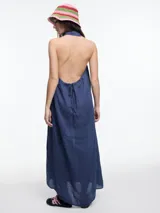 Vestido largo de lino en color azul, con cuello camisero, cierre frontal de botones y espalda descubierta con diseño estilo halter. Presenta un bordado decorativo en el cuello y bolsillos laterales.