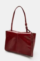 Bolso formato mini shopper de piel con acabado brillante y efecto arrugado. Cuenta con doble compartimento, cierre mediante botón imantado, bolsillo interior y asa de hombro ajustable.