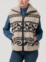 Chaleco de polar con diseño jacquard de motivos geométricos en tonos beige y gris oscuro. Presenta cuello alto, cierre frontal metálico con bordes de cuero sintético y bolsillos laterales con cierre.