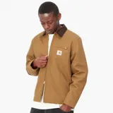 Chaqueta Carhartt modelo Detroit, color tostado, con cuello de pana en contraste, cierre frontal con cremallera, bolsillo en el pecho con cremallera y logo de la marca bordado.
