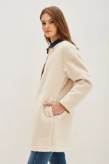 Saco de corte recto confeccionado en tejido tipo boucle color crema, con terminaciones en contraste color marrón y cierre frontal con botones metálicos.