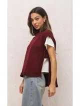 Chaleco tejido de punto en color bordó, con cuello alto y diseño de silueta amplia. Presenta aberturas laterales pronunciadas y un largo asimétrico, siendo más corto en la parte delantera y más largo en la espalda.